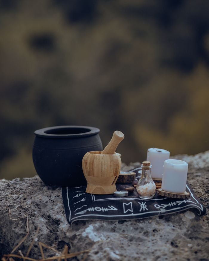 About A rustic setup with a mortar, candles, and pot on a rock surface outdoors.